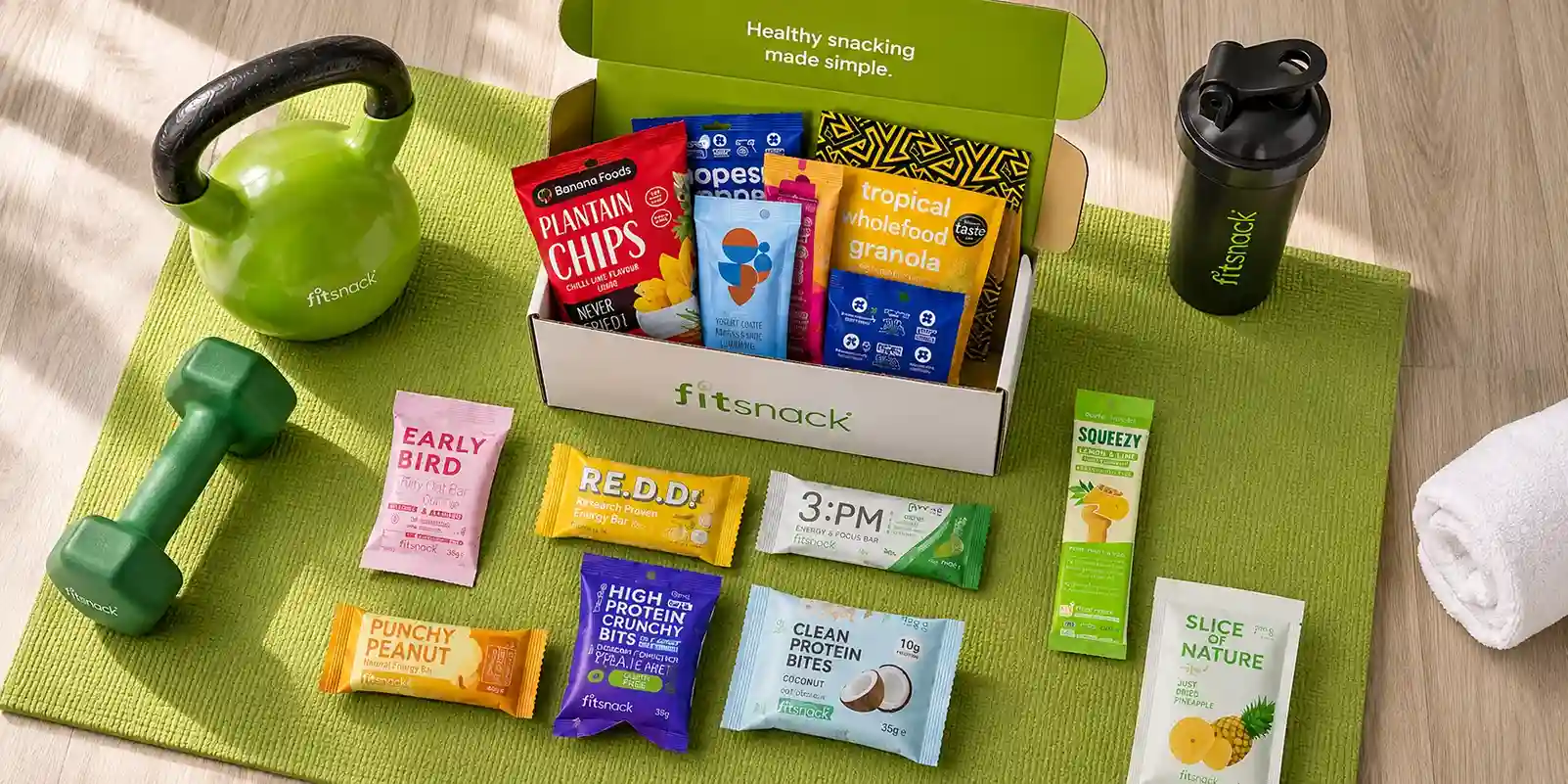 FitSnack subscription box with high-protein snacks on a yoga mat next to dumbbells